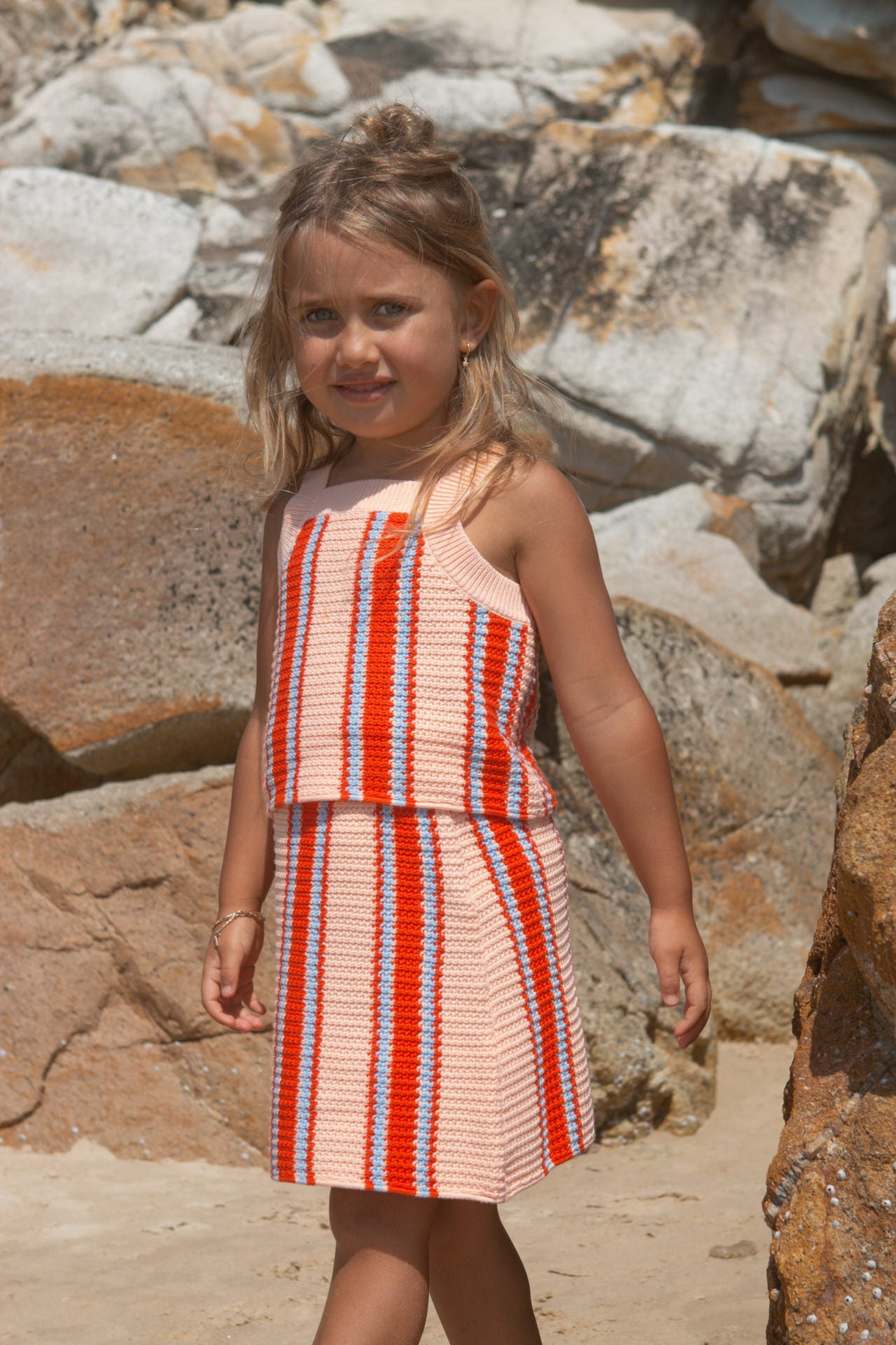 Young girl in a striped top and skirt standing among rocks