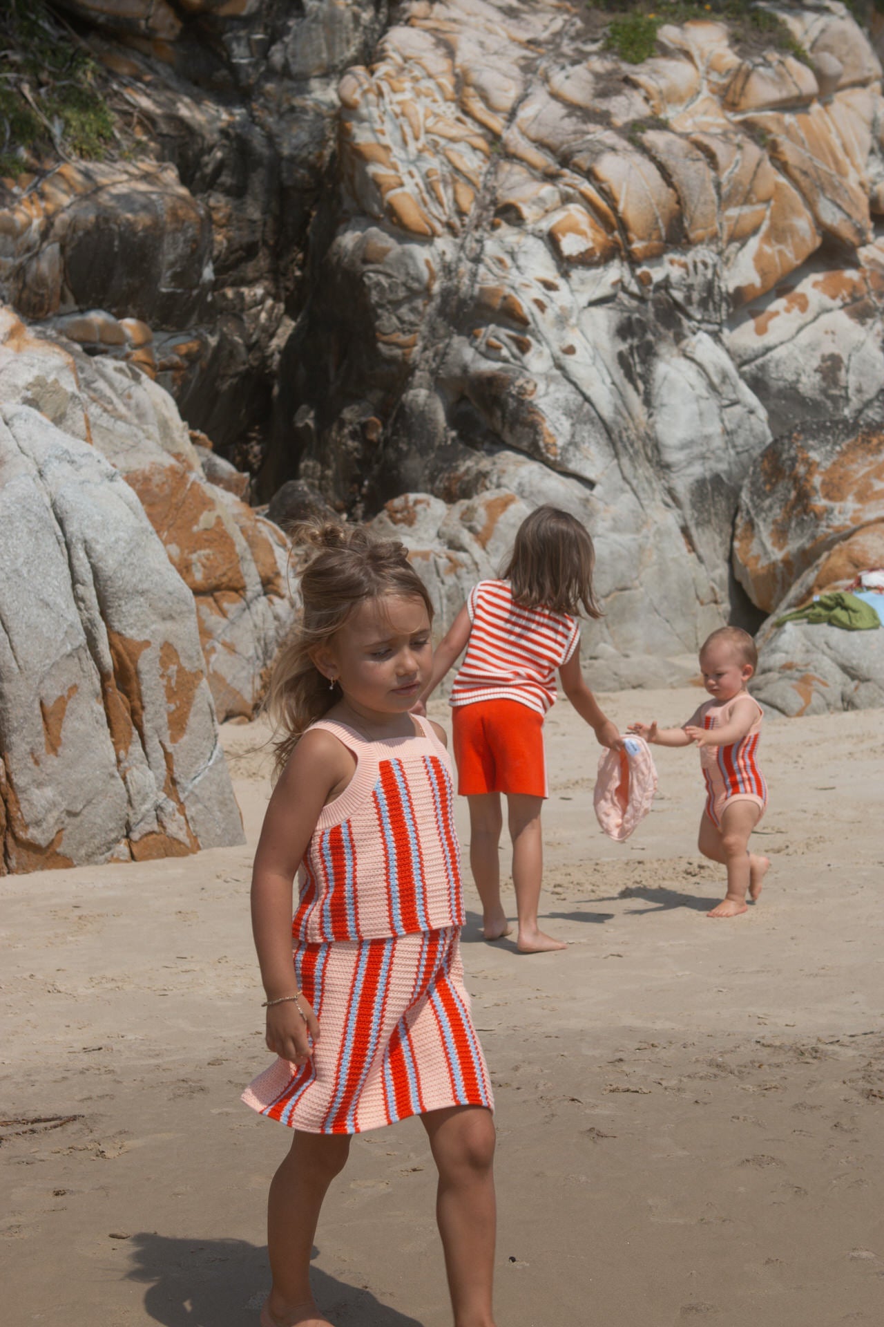 Children in matching red and white outfits playing on a rocky beach.