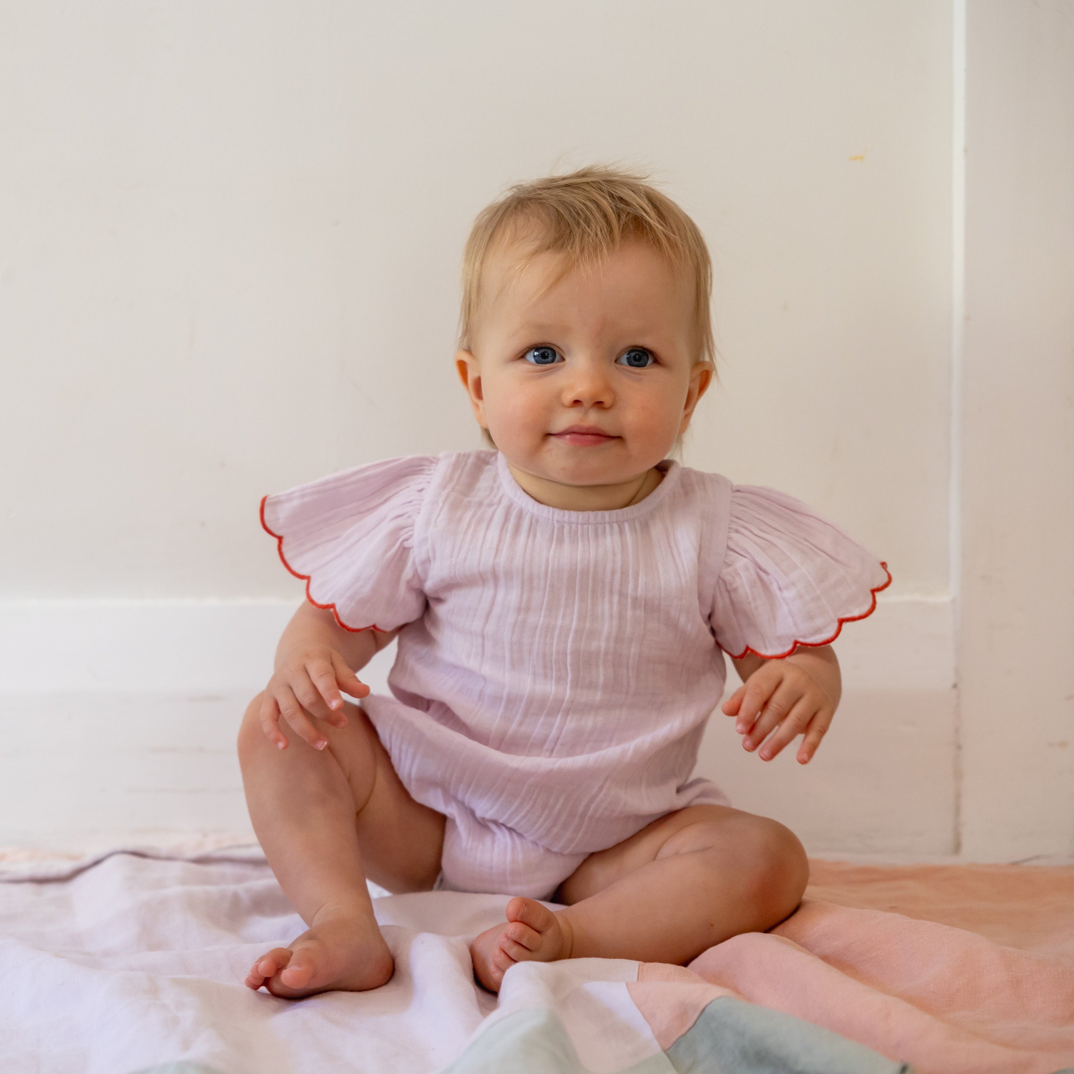 Baby sitting on a bed wearing a pink ruffled outfit.