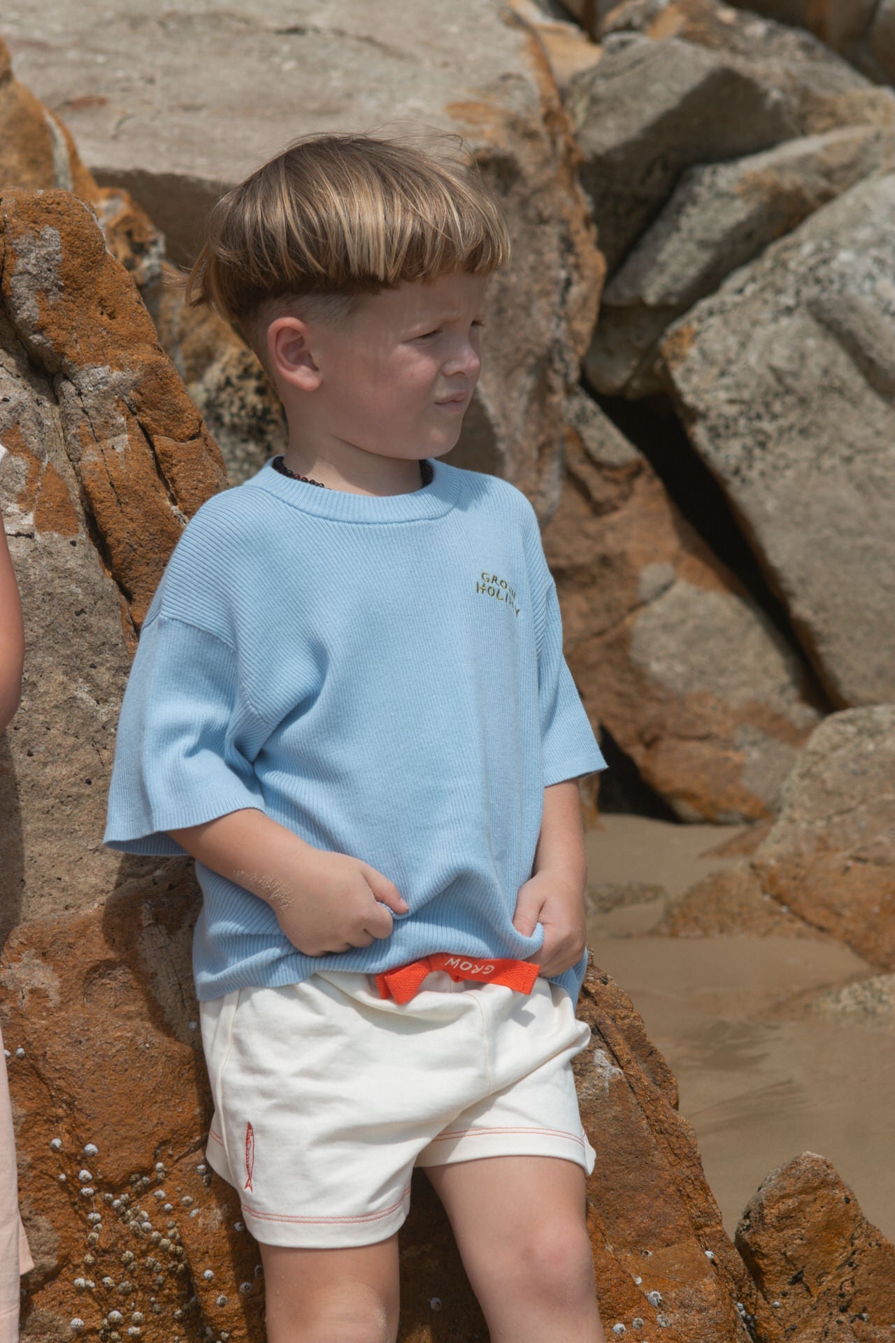 Young boy in a blue shirt and white shorts standing on rocky terrain.